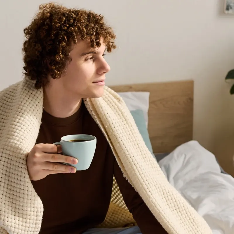 A person sitting wrapped in a blanket holding a warm mug, conveying the importance of pausing and being gently present with difficult emotions