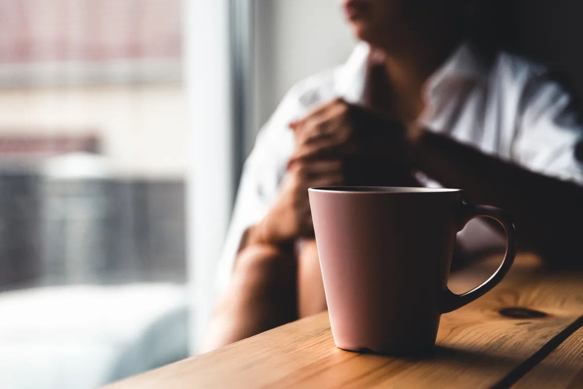 Person sitting quietly at a table with a cup of tea, looking inward