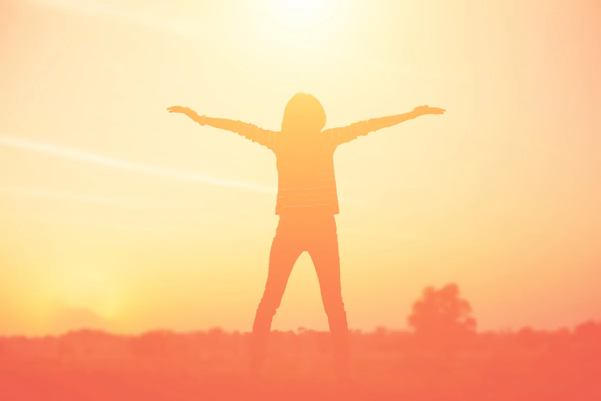 A person standing with arms open to the sky in a natural setting, conveying receptivity, peace, and alignment with purpose
