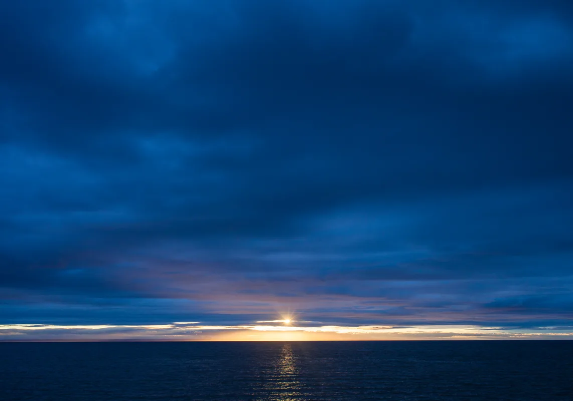 Dawn just beginning to break over a calm, open landscape — the transition from dark to the very first light of morning