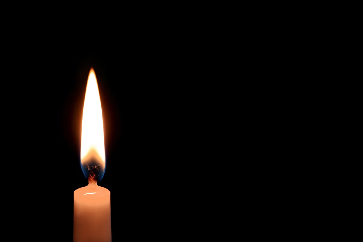 A single steady candle flame burning in a dark room — quiet focus and the simple act of shedding light on what was previously hidden